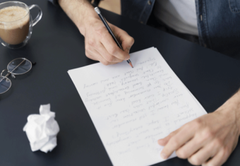 une personne écrit une lettre de motivation à la main sur une table avec un brouillon froissé à côté d'elle