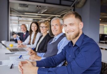 cinq hommes et femmes professionnels souriants assis à une table de conférence dans un bureau