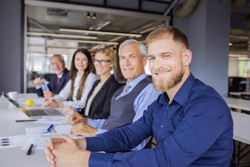 cinq hommes et femmes professionnels souriants assis à une table de conférence dans un bureau